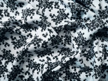 Kumaşın deseni ve arkaplanı beyaz ve küçük siyah bir çiçek motifi var.