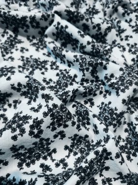 Kumaşın deseni ve arkaplanı beyaz ve küçük siyah bir çiçek motifi var.