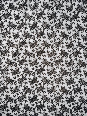 Kumaşın deseni ve arkaplanı beyaz ve küçük siyah bir çiçek motifi var.
