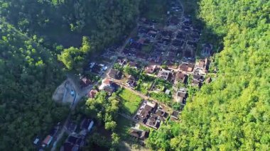 Tepeler ve yemyeşil ağaçlarla çevrili kırsal bir manzara.