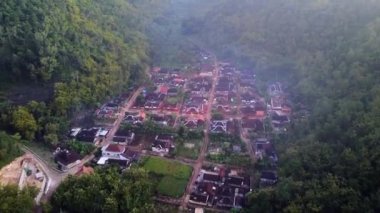 Tepeler ve yemyeşil ağaçlarla çevrili kırsal bir manzara.