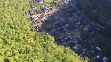 Tepeler ve yemyeşil ağaçlarla çevrili kırsal bir manzara.