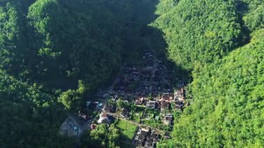 Tepeler ve yemyeşil ağaçlarla çevrili kırsal bir manzara.