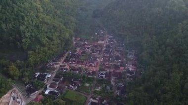 Tepeler ve yemyeşil ağaçlarla çevrili kırsal bir manzara.