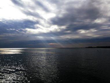 Deniz manzarası, güneş ışığı bulutların arasında parlıyor ve deniz yüzeyine vuruyor..