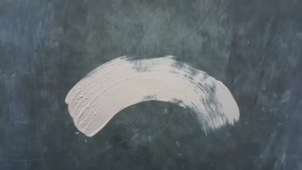 Gri bir yüzeyde beyaz bir boya fırçası. Fırça darbesi uzun ve ince ve yüzeydeki tek iz.