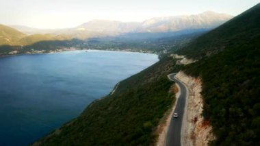 Ağaçlık dağların arasında dolambaçlı bir yol manzarası, sakin bir göl sol taraftaki güzelliği zarifçe yansıtıyor..