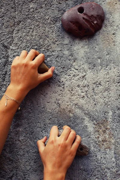 Close-up of female hands holding rock climbing equipment on gray wall