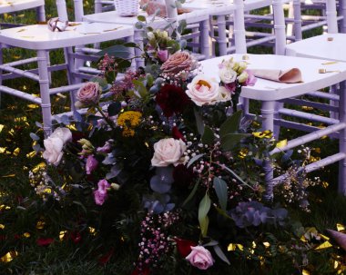 Çiçekler, güller ve yeşilliklerle süslenmiş düğün sandalyeleri.