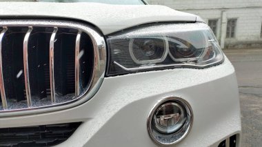Dnipro, Ukrayna - 09 Nisan 2025: Far, sis ışığı ve krom ızgara üzerine yağmur damlaları konmuş beyaz BMW araba önü kapatın. Lüks araç kavramı, yağmurlu hava, otomotiv ayrıntıları, modern tasarım.