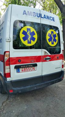 Dnipro, Ukrayna - 26 Nisan 2025 - Ağaçlı caddeye park edilmiş tıbbi sembollü ambulansın arka görüntüsü. Acil servis konsepti, sağlık hizmetlerine hazırlık, kentsel güvenlik önlemleri. Dikey.