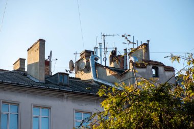 Tarihi bir Avrupa binasında eski bacaları ve modern uydu antenleri olan kaotik bir şehir çatısı. Yüksek kalite fotoğraf