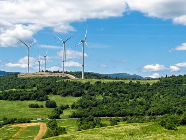 Yenilenebilir rüzgar enerjisi türbinleri orman dağları ve dağınık beyaz bulutlarla yemyeşil vadide dimdik ayakta duruyor. Yüksek kalite fotoğraf