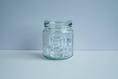 Cam bir kavanozda beyaz arka planda birkaç buz küpü var..