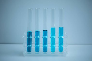 5 mavi test tüpü beyaz arkaplan ve tıbbi konsepte sahip tıbbi bir askıya yerleştirilmiş..