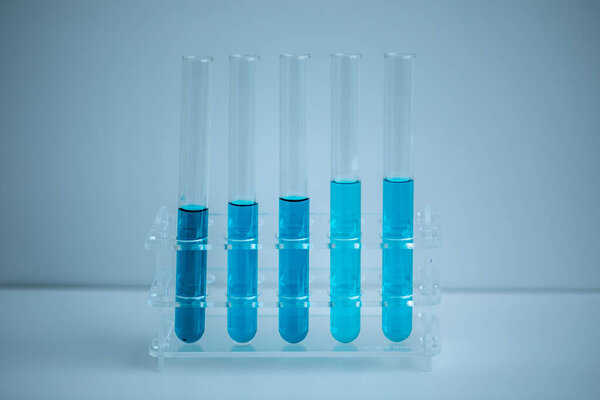 5 синих пробирки помещены в стойку медицинских труб с белым фоном, медицинская концепция.