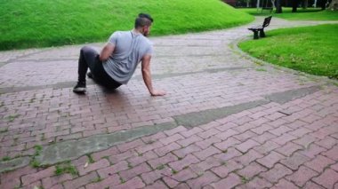 Genç adam şehir parkında dört ayaklı egzersizler yapıyor.