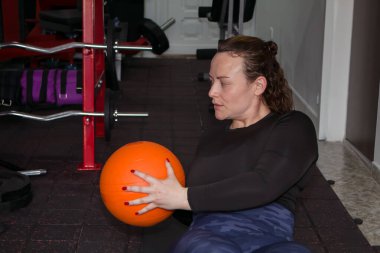 Sportif bir kadın spor salonunda ağır bir topla egzersiz yapıyor.