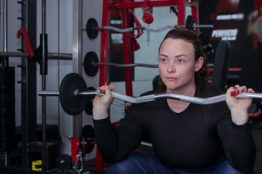 Spor salonunda ağırlık plakasıyla egzersiz yapan sporcu bir kadın.