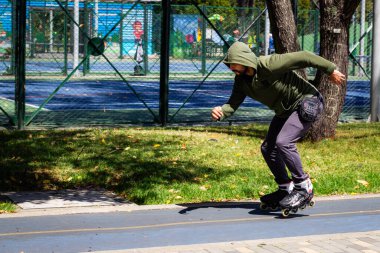 Şehirdeki bir parkta paten kayan genç bir adam.