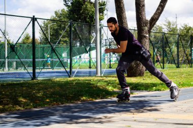 Şehirdeki bir parkta paten kayan genç bir adam.