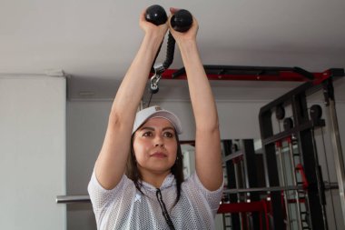 Sportif bir kadın spor salonunda kol ve omuz kasları için egzersiz yapıyor. Spor salonunda spor yapmak.