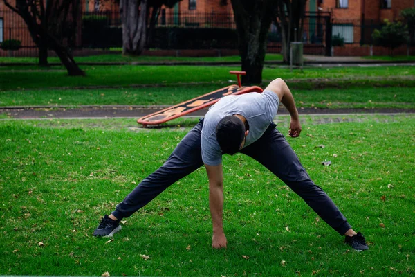 Genç sporcu şehirdeki bir parkta fiziksel antrenman yapmak için esneme hareketleri yapıyor.