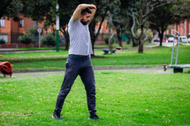 Genç sporcu şehirdeki bir parkta fiziksel antrenman yapmak için esneme hareketleri yapıyor.