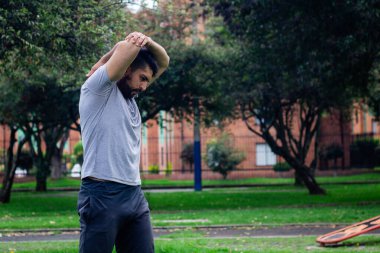 Genç sporcu şehirdeki bir parkta fiziksel antrenman yapmak için esneme hareketleri yapıyor.