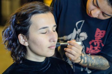 Soyunma odasında profesyonel bir makyöz tarafından makyaj yapılan genç bir kadın.