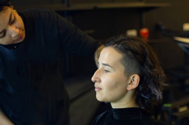 Soyunma odasında profesyonel bir makyöz tarafından makyaj yapılan genç bir kadın.