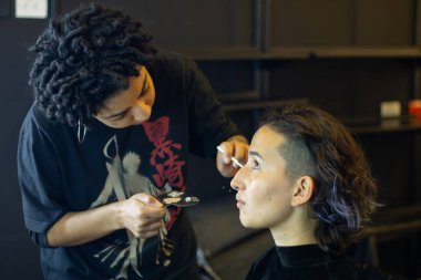 Afro makyöz kadın soyunma odasında genç bir mankene makyaj yapıyor.