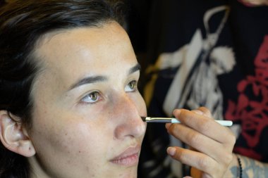 Soyunma odasında profesyonel bir makyöz tarafından makyaj yapılan genç bir kadın.