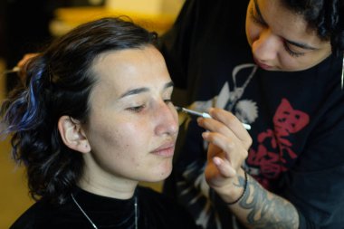 Soyunma odasında profesyonel bir makyöz tarafından makyaj yapılan genç bir kadın.