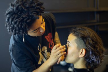 Soyunma odasında profesyonel bir makyöz tarafından makyaj yapılan genç bir kadın.