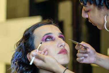 Profesyonel makyöz tarafından soyunma odasında makyaj yapılan genç bir kadın.