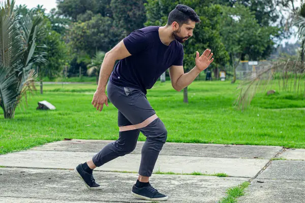 young man training with elastic bands, doing arm exercise outdoors in a park