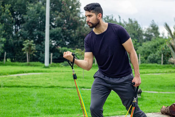 Lastik bantlarla antrenman yapan genç bir adam, parkta kol egzersizi yapıyor.