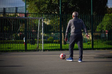 Mutlu emekli adam, öğleden sonra parkta futbol oynarken topa vuruyor.