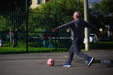 Mutlu emekli adam, öğleden sonra parkta futbol oynarken topa vuruyor.