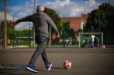 Mutlu emekli adam, öğleden sonra parkta futbol oynarken topa vuruyor.