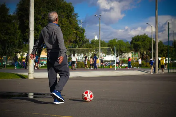 Mutlu emekli adam, öğleden sonra parkta futbol oynarken topa vuruyor.