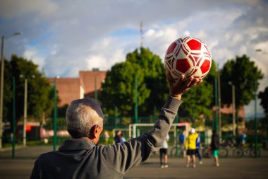 Emekli yaşlı bir adam parktaki bir futbol sahasında kalecilik yapıyor.