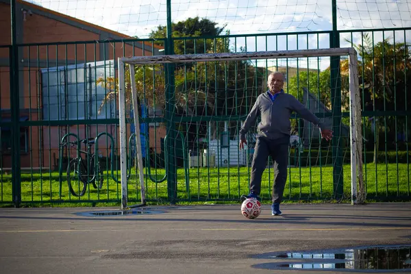 Mutlu emekli adam, öğleden sonra parkta futbol oynarken topa vuruyor.