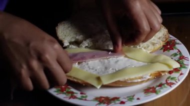 Fırıncı kadının elleri, mutfak masasında marul, jambon ve peynirli lezzetli bir sandviç hazırlıyor.