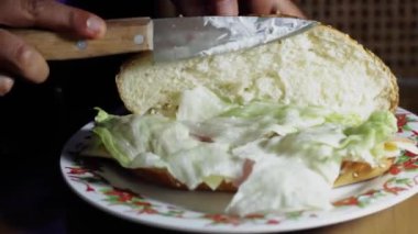 Fırıncı kadının elleri, mutfak masasında marul, jambon ve peynirli lezzetli bir sandviç hazırlıyor.