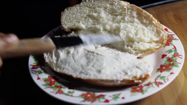 女性の手は 台所のテーブルの上の皿にサンドイッチを準備するパンにナイフでバターを塗ります — ストック動画
