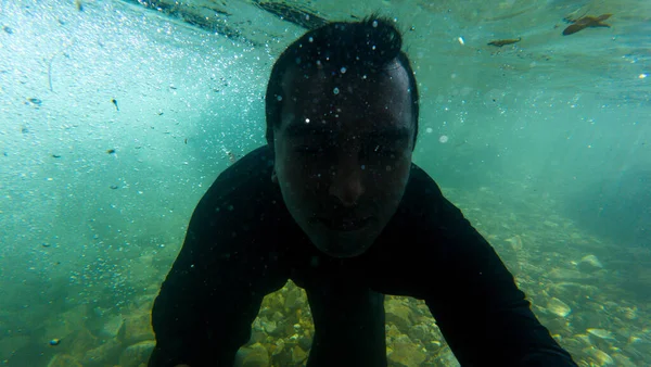 man swimming underwater in a deep river with bubbles and stones at the bottom of the sea