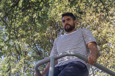 Parkta barda egzersiz yapan çekici bir genç adam kol egzersizi yapıyor.