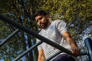 Parkta barda egzersiz yapan çekici bir genç adam kol egzersizi yapıyor.